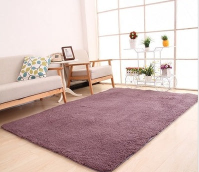 Purple rug on a light wooden floor with a couch and decorative items in the background.