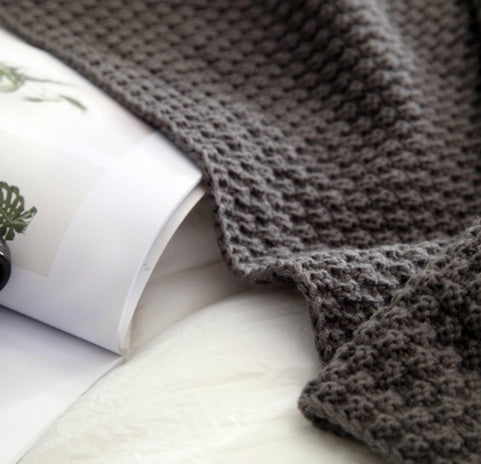 Gray knitted blanket draped over a white surface with a magazine underneath