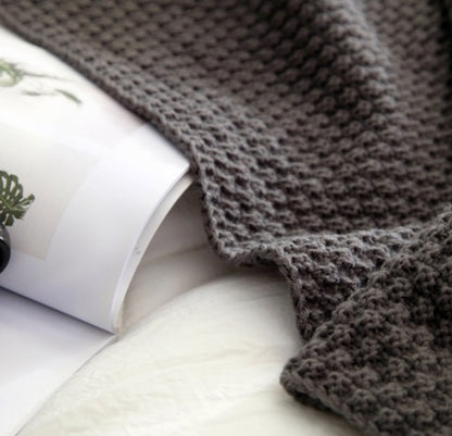 Gray knitted blanket draped over a white surface with a magazine underneath