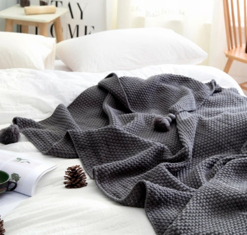 Gray knitted blanket on a white bed with a cozy bedroom setting.