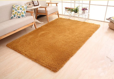 Brown rug on a light wooden floor with a neutral-colored sofa and decorative items in the background.