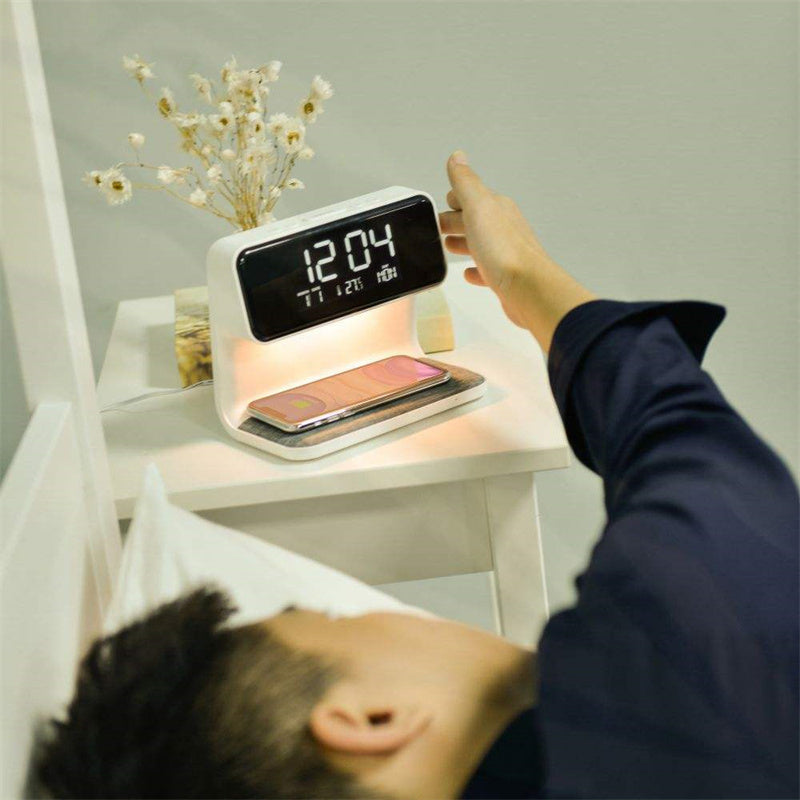 Person using a digital alarm clock on a nightstand with a smartphone below.