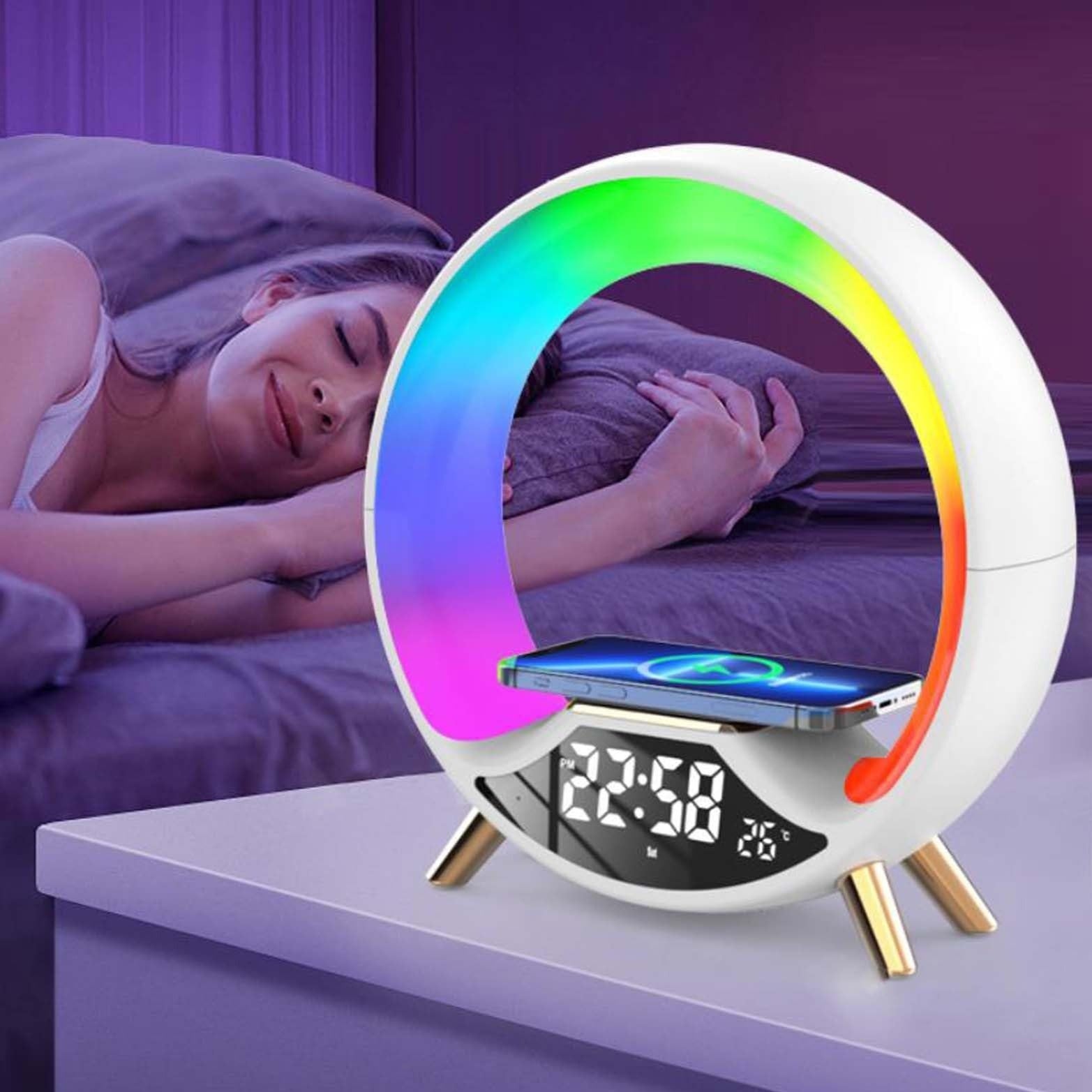 Multicolored night light with digital display and phone stand on a surface, with a person lying in bed in the background.