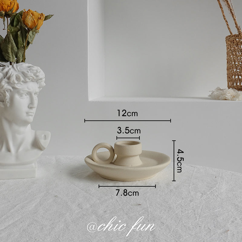 Small ceramic cup and saucer with dimensions on a textured surface, next to a bust and flowers.