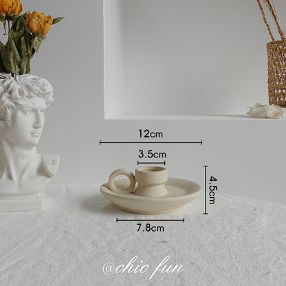 Small ceramic cup and saucer with dimensions on a textured surface, next to a bust and flowers.