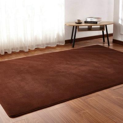 Brown rug on a wooden floor with a small table and books in the background.